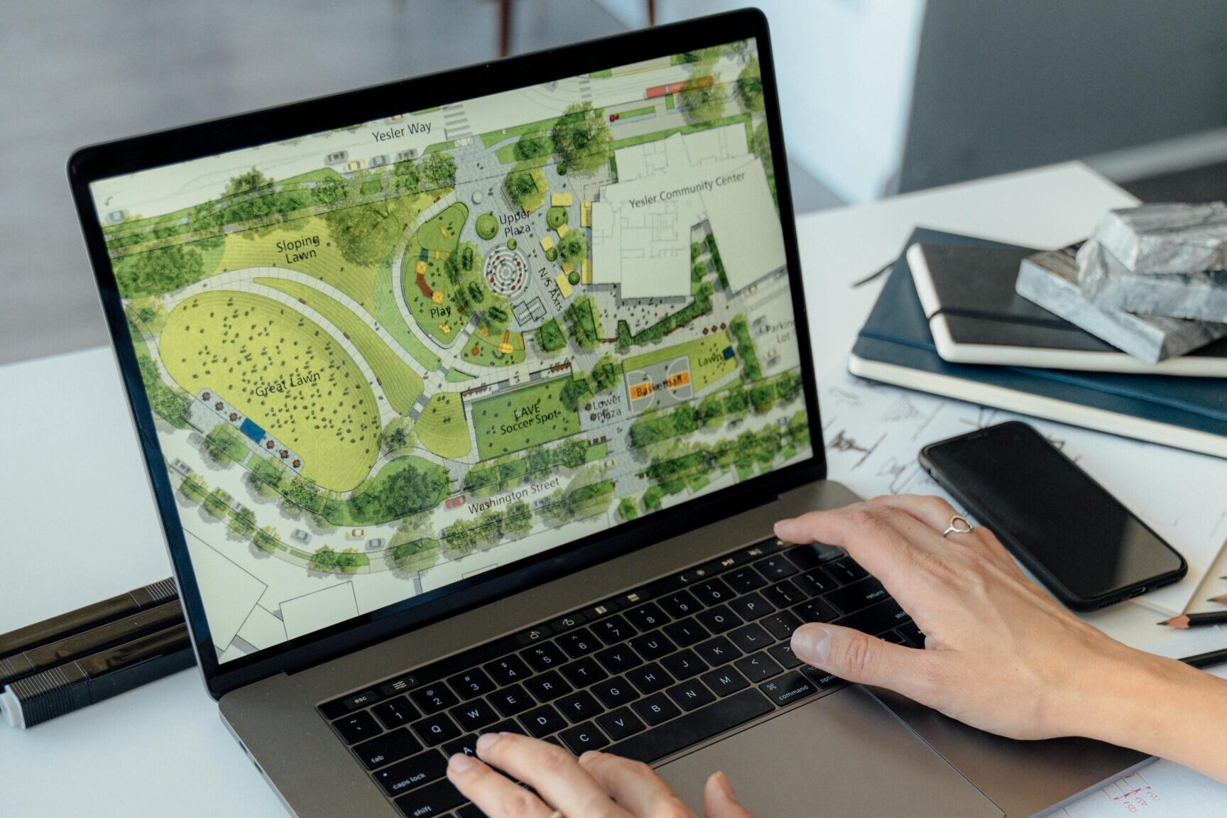 Architect working on landscape plan displayed on laptop with hands typing on keyboard.